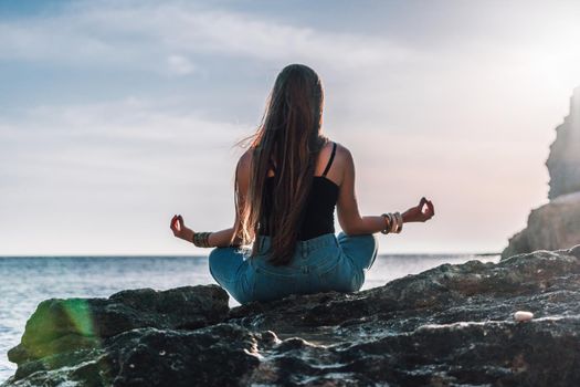 Young woman in swimsuit with long hair practicing stretching outdoors on yoga mat by the sea on a sunny day. Women's yoga fitness pilates routine. Healthy lifestyle, harmony and meditation concept.