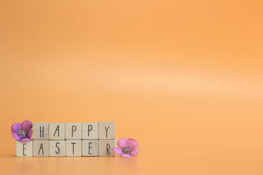 Happy Easter Holiday text on bright orange pastel colored background with purple spring flowers, concept for greeting card,spring,Easter with copy space space for text