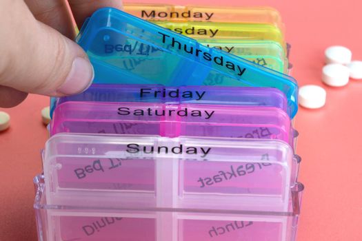 Pill box reminder, hand taking medicine daily pills in colorful box on pink background, elderly,senior,business,health,medication concept modern design close up