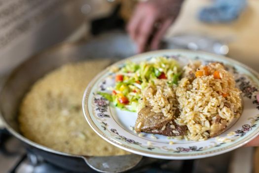 Large cauldron with freshly cooked rice. A series of the process of cooking pilaf in a huge cauldron on open fire. Frying onions and vegetables, adding meat. Appetizing pilaf cooked in a cauldron