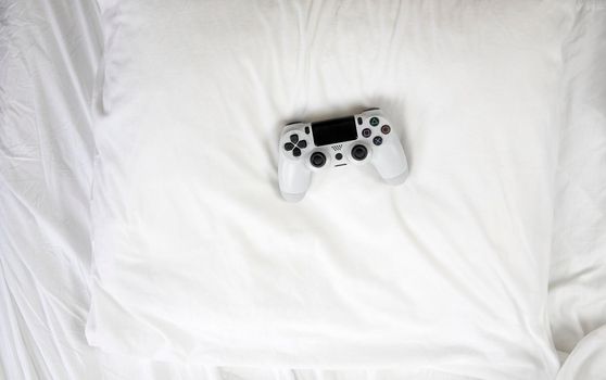 Closeup image top view game controller, lying on white sheets of bed at home with copy space concept