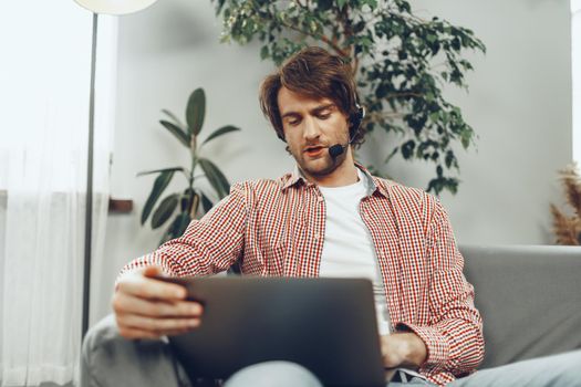 Young man wearing headset doing a video call by laptop at home