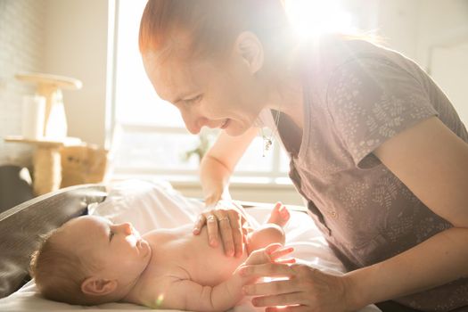 Smiling caring woman looking at her little baby with her hands on his stomach. Mid shot