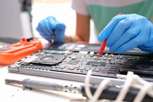 Laptop repair, gloved hands holding a voltage meter for electronics. Processor testing, diagnostics motherboard