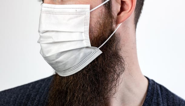 Caucasian young bearded adult man wearing a protective or surgical mask to avoid pollution and contagious virus and diseases isolated on white background, Covid-19, coronavirus,health,beard, epidemic concept close