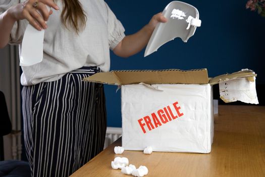Young woman opening damaged delivery package,online shopping package. Broken fragile plate at home unhappyy