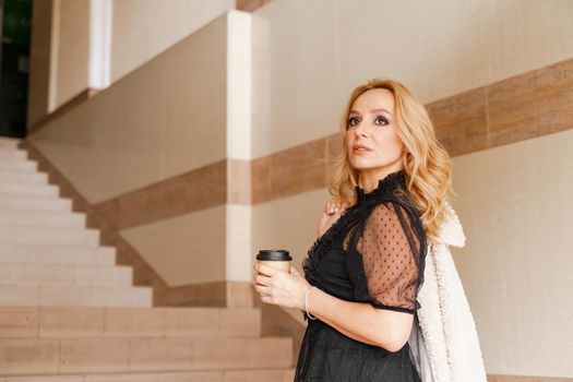 Portrait of a beautiful smiling blonde. She's walking up the stairs, coffee in hand. The Concept Of Urban Life