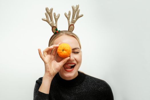 Beautiful Santa girl with reindeer antlers. Happy blonde in a black sweater has closed her tangerine eye and shows her tongue.