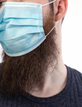 Caucasian young bearded adult man wearing a protective or surgical mask to avoid pollution and contagious virus and diseases isolated on white background, Covid-19, coronavirus,health,beard, epidemic concept close