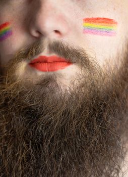 Young handsome bearded man with pride flag on his cheek, rainbow flag standing for LGBTQ, Gender right and sexual minority. Portrait closeup