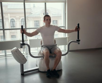 Modern gym - a guy sitting on the strength training machine. Mid shot