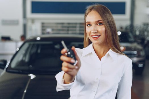 Young happy woman buyer/seller near the car with keys in hand close up