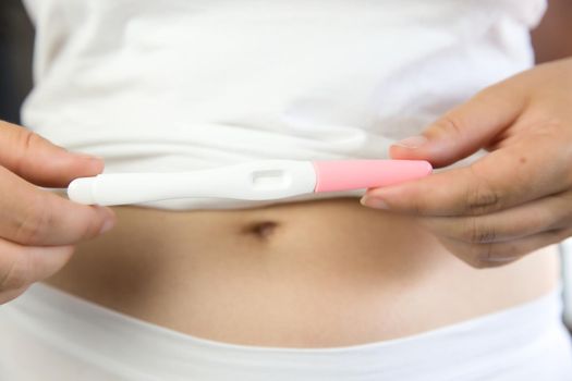Young women wearing white underwear with hand holding blank pregnancy test and belly. closeup copy space