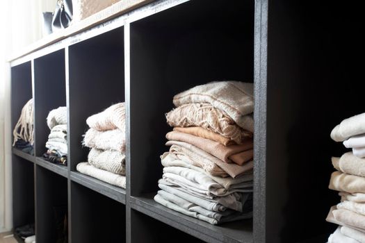 Open wardrobe with lots of folded clothes, organized closet with piled up clothes modern and clean interior of luxury home closeup