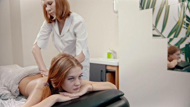 Young ginger woman with blue eyes having a massage treatment - indoor