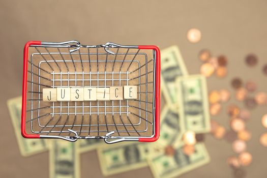 Justice written with wooden cubes in iron shopping basket with Money coins and bills on the background, Business,law,justice,Financial concept space for text closeup