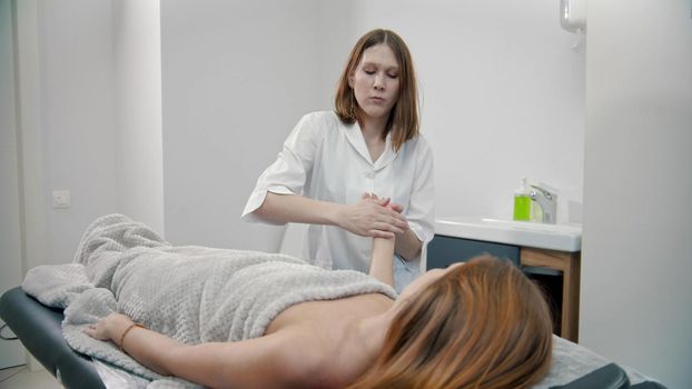 Woman therapist giving a massage for palms and fingers of a young woman - indoor