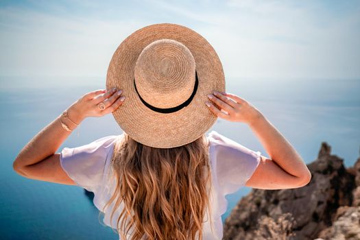 Woman enjoying summer beach vacation on the background of the ocean. A woman adjusts her straw hat on her head while sitting facing the sea
