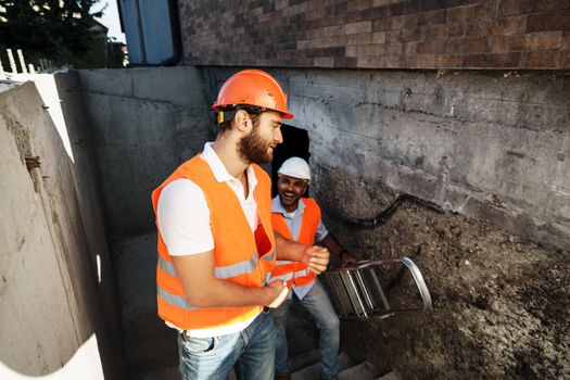 Two young male engineers in uniform and hardhats working at construction site, close up