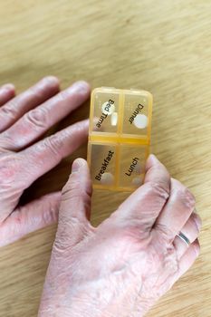 Closeup of an elderly senior woman's hands taking her medication for the week in a pill box on wooden table, business,health concept close up