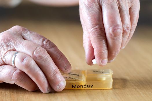 Closeup of an elderly senior woman's hands taking her medication for the week in a pill box on wooden table, business,health concept close up