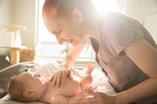 Smiling caring mother looking at her little baby with her hands on his stomach. Mid shot