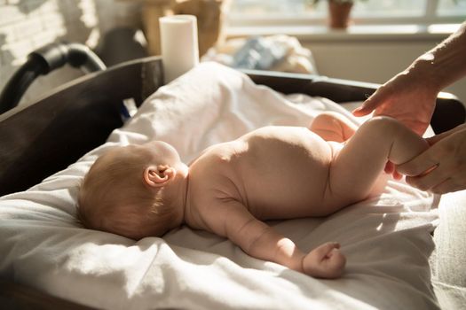 A little baby lying on a bed on white sheets and his parent holding his legs. Mid shot