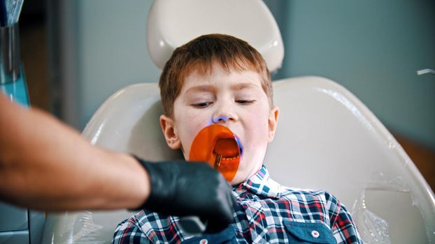 A little boy having his tooth done - putting the photopolymer lamp in the mouth. Mid shot