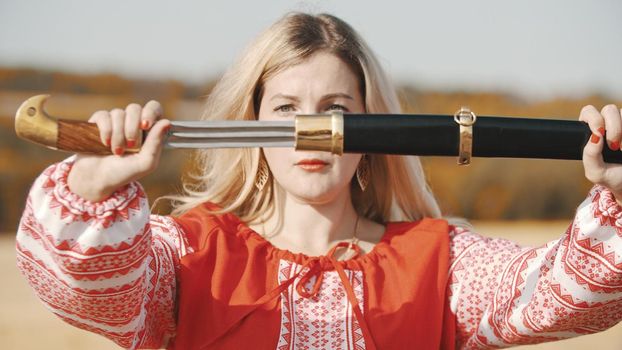Feisty woman in red dress pulls out a sword out of the sheath. Mid shot
