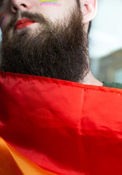 Young handsome bearded man with pride flag on his cheek, rainbow flag standing for LGBTQ, Gender right and sexual minority. Portrait closeup