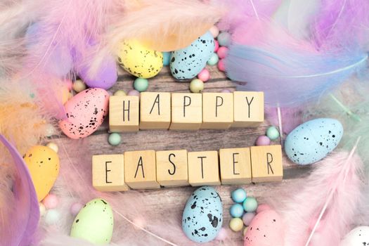 Happy Easter written with wooden cubes surrounded with beautiful pastel colored decorative feathers and eggs, April, Easter, Religion, Spring concept for background and greeting card top view bright colors