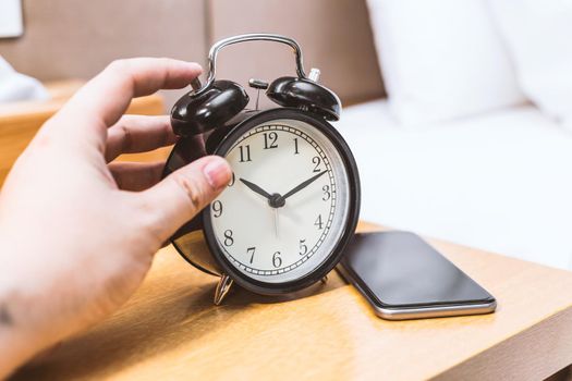 Man lying in bed turning off an alarm clock in the morning