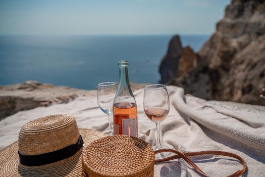 A picnic blanket, champagne, two glasses, a hat and a straw purse. Top on the mountain against the background of the sea and rocks in the sea