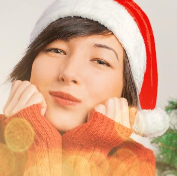 Portrait of smiling young woman in Santa hat. Christmas or New Year celebration. Image with light effect