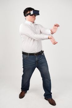 Man wearing virtual reality goggles watching movies or playing video games. He is isolated on a white background. The vr headset design is generic and no logos.