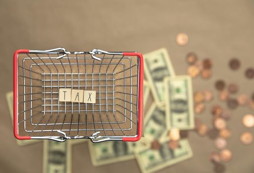 Tax written with wooden cubes top view in shopping basket with money coins and bills on the background. Business and financial concept Copy space