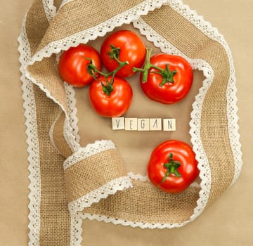 Vegan written with wooden cubes near fresh red tomatoes with brown craft paper background, surrounded with natural burlap ribbon, Vegan, Vegetarion, Healthy food concept copy space top view