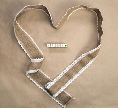 Flat lay design,natural burlap ribbon in heart shape with the text VEGAN written and craft paper background texture, top view, Healht, Vegan, Vegetarian concept closeup