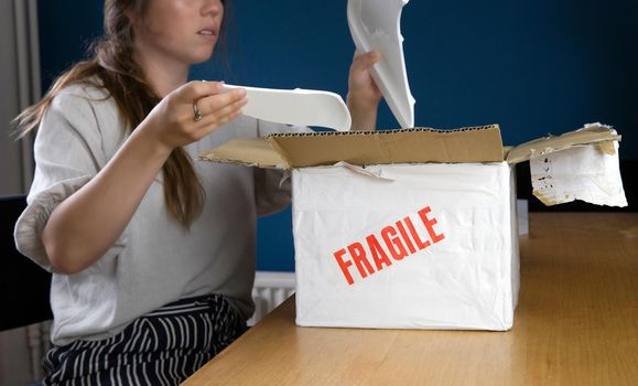 Young woman opening damaged delivery package,online shopping package. Broken fragile plate at home unhappyy