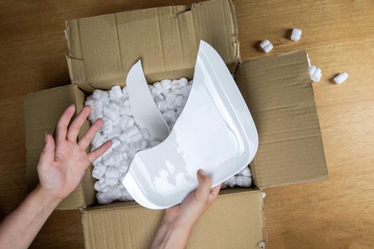 Broken plate in damaged cardboard box top view, damaged home delivery unpacking box close up