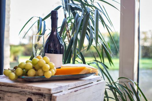 cheese platter with grapes and wine on a table near a window with a cozy chair. Modern interior design luxury decoration, food and interior concept tasty