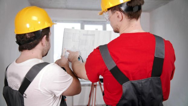 Two men workers looking at the layout of new apartment. Mid shot