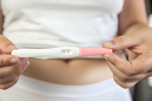 Young women wearing white underwear with hand holding positive result pregnancy test and belly. closeup