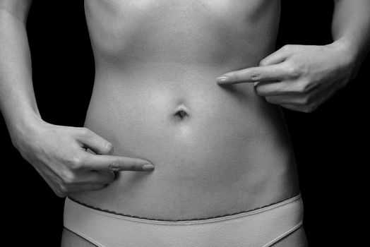 Unrecognizable woman points to the abdomen, monochrome image. Space for text on the abdomen
