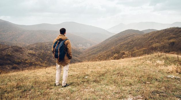 Hiker man with backpack standing on hill and enjoying by scenic of mountains, rear view