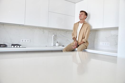 Happy handsome man is standing on minimalistic kitchen and smiling