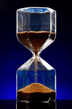 Hourglass illuminated on dark blue background close up photo