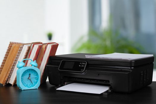 Stack of books and home printer against blurred background, close up