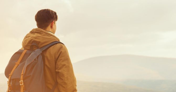 Hiker man with backpack enjoying landscape of mountains, rear view