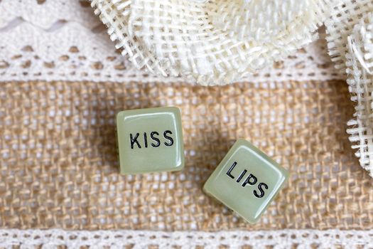 Two erotic dice for sexual game with cotton lace background texture, with the text Kiss lips for Valentines Day,sex,sensual,romantic, love concept close up